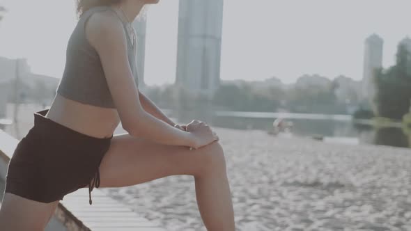 Attractive Slim Girl Wearing a Medical Mask Stretching Her Legs Near the River