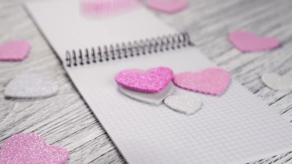 Glittering paper hearts fall on an open notebook with black metal binding 