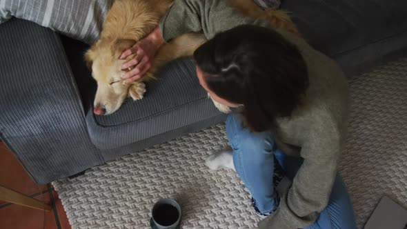 Smiling caucasian woman stroking her pet dog on sofa next to her