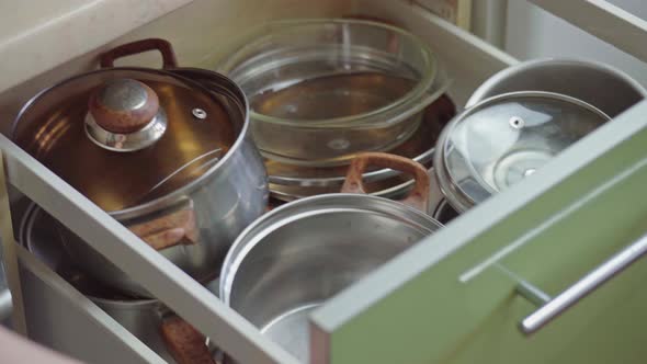 Man hand opening kitchen cupboard door and taking pot by shelf inside