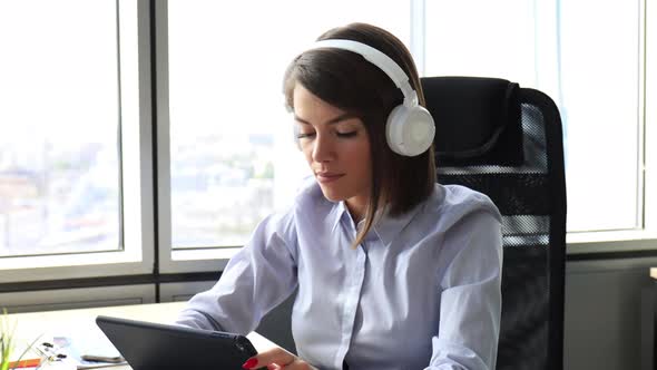 Young attractive smiling caucasian woman using tablet sitting at modern office, singing song