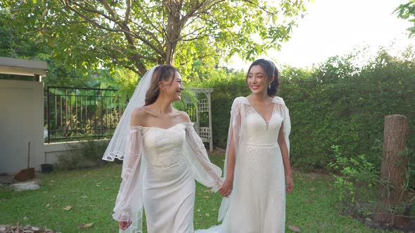 4K Portrait of Asian lesbian couple in wedding dress holding hands walking together in the garden.