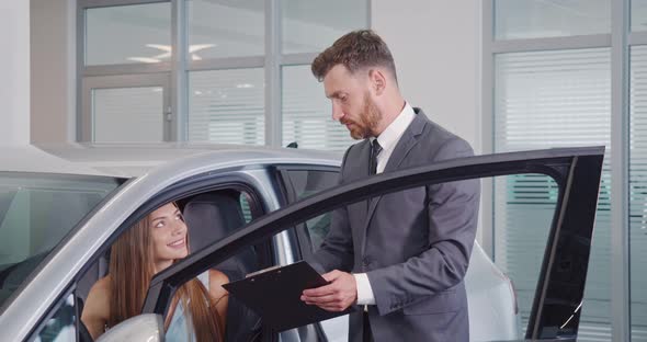 Car Dealer Showing Female Buyer New Auto at Salon