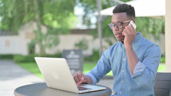 African Man Talking on Smartphone in Outdoor Cafe