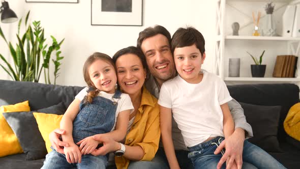 Classic Portrait of Happy Lovely Family of Four Sitting on Sofa in Cozy Living Room