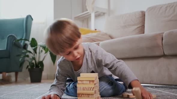 Child Builds a Wooden Tower for Playing Jenga Sitting on the Floor at Home