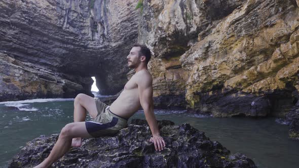 Handsome attractive male sitting on a rock in the sea.