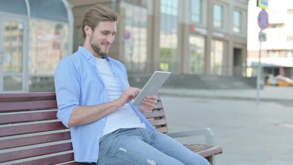 Man Celebrating Online Win on Tablet While Sitting Outdoor on Bench