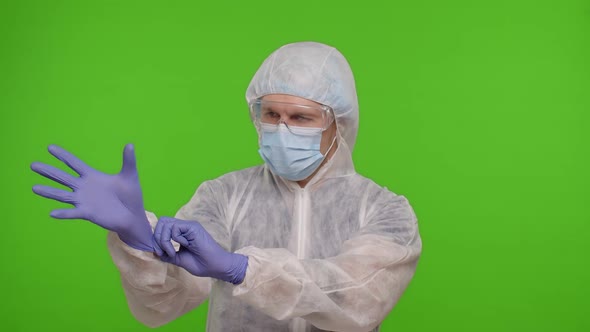 Healthcare Worker Doctor Standing on Chroma Key and Puts on Gloves and Mask Coronavirus Pandemic