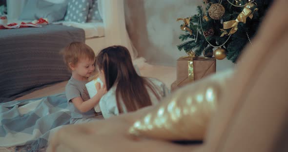 Girl Gives the Boy a New Gift. Boy Shakes a Box with a Gift and Listens To What's Inside