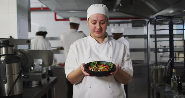 Portrait of caucasian female chef presenting dish and looking at camera