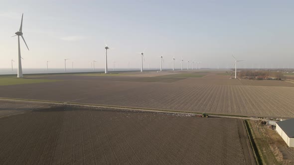 Aerial rural scene, Birds follow tractor plowing on endless field with wind turbines Landscape