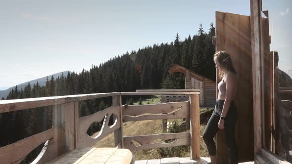 Woman comes out of a wooden hut with mountain view in the morning