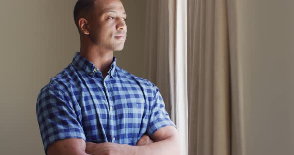 Thoughtful biracial man standing at window and looking into distance