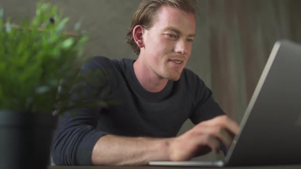 Smiling Young Man of Business Sitting at Computer and Typing at Laptop Messages