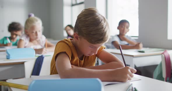 Video of focused caucasian boy sitting at desk in classsroom