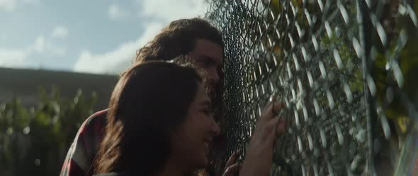 A boy and a girl looking at the banana trees behind the metal fence