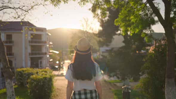 Woman in a straw hat, walking forward. Rear view.Sunset in the background.