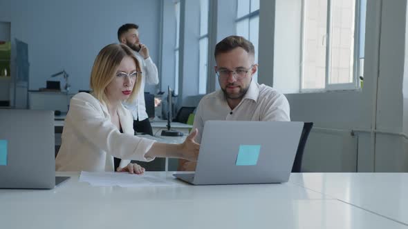 Two Coworkers in Glasses Sit and Watch in the Laptop Screen