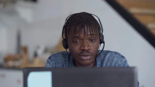 Front View Closeup Portrait of African American Young Man in Earphones Talking at Laptop Web Camera