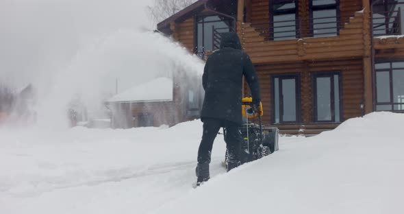 Man Removes Snow with Snowblower in Yard at Snowfall in Slow Motion