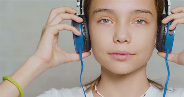 Teenage Girl Puts on Headphones Looking at Camera and Smiling