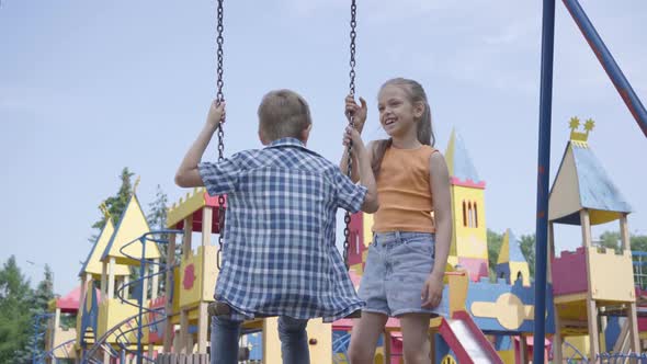 Cute Girl with Long Hair Swinging on a Swing Cute Boy Outdoors. Couple of Happy Children. Funny