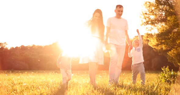 Happy Family Their Man with Two Children Walking on the Field at Sunset in the Sunset Light in the