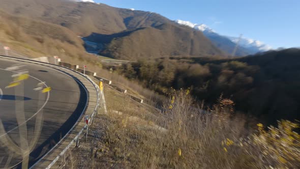 FPV Drone Side Follow Red Car Driving on Serpentine Road Top Mountain to Touristic Resort Valley