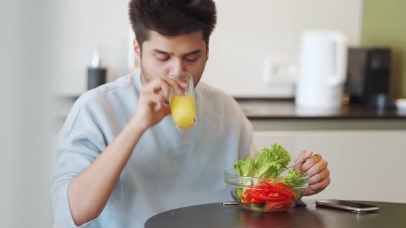 Serious Indian man wearing sweatshirt eating salad and looking at the phone