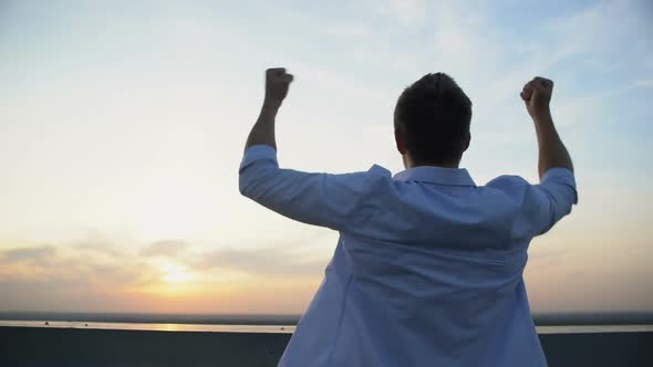 Back View of Caucasian Man Raising Hands to Sky on Sunset Background, Motivation
