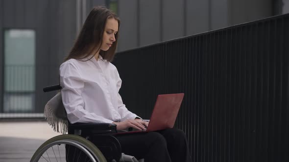 Young Professional Beautiful Disabled Woman Sitting in Wheelchair Messaging Online on Laptop