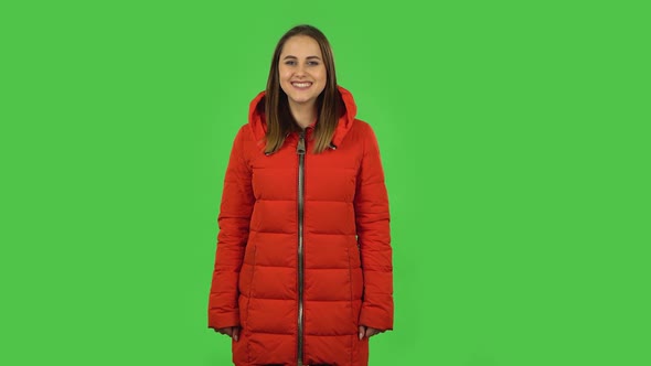 Lovely Girl in a Red Down Jacket Is Smiling While Looking at Camera . Green Screen