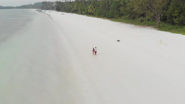 Aerial: couple on vacation walking on exotic beach romantic sky at sunset Pasir