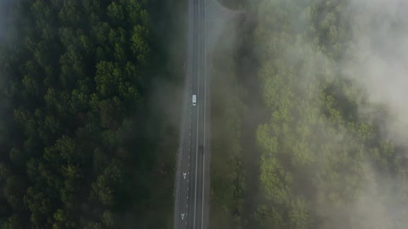 Aerial View of Driving Cars on the Road in the Forest Through the Clouds