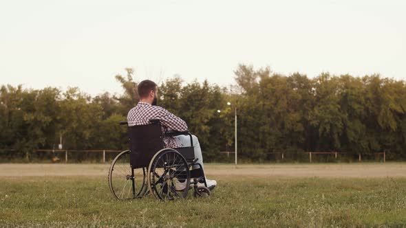 Sad Disabled Man is Sitting in Field in Wheelchair and is Sad Reflecting on His Diagnosis Back View