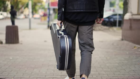 Man Walk Down the Street Holding a Guitar Case