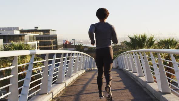 Rear view of fit african american man exercising outdoors in city, running on footbridge