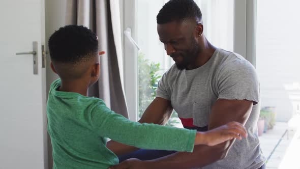 African american father helping his son with getting dressed in bedroom