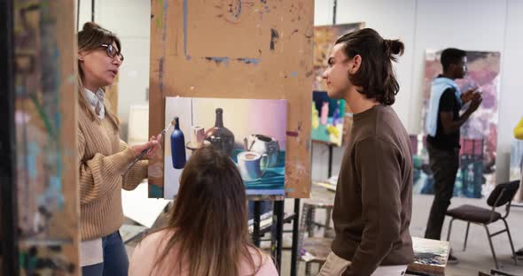 Mature teacher working with art students during painting class at school