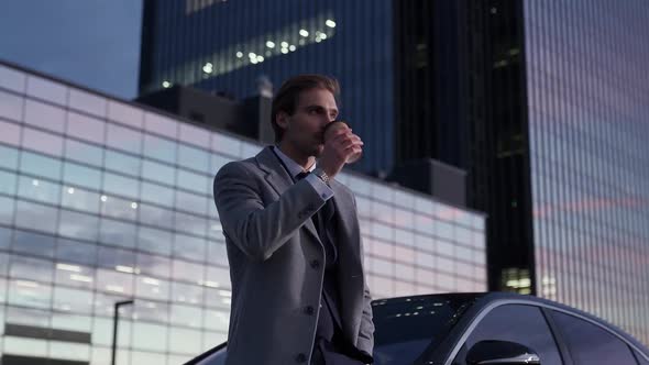 Portrait of a Cheerful Businessman Standing Near a Business Car and Drinking Coffee Top Manager in a