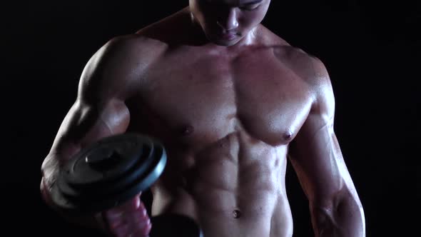 Asian Bodybuilder Training Biceps with a Dumbbells. Black Smoke Background. Slow Motion