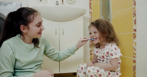 Little Two Sisters Brushing Their Teeth Each Other Intensely in the Bathroom