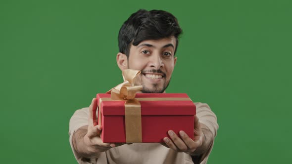 Hispanic Happy Man Giving Gift Large Red Box with Gold Ribbon Studio Green Background Portrait