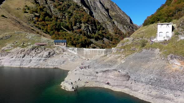 Lac d'Oô lake in the French Pyrenees with visitors exploring the dam wall on cliffside, Aerial orbit