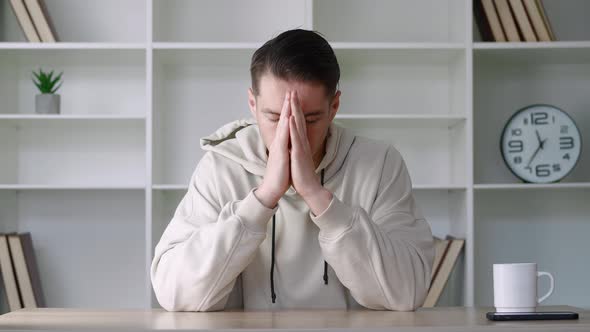 Pensive Man Holding Hands in Namaste Gesture Sitting at Desk with Eyes Closed