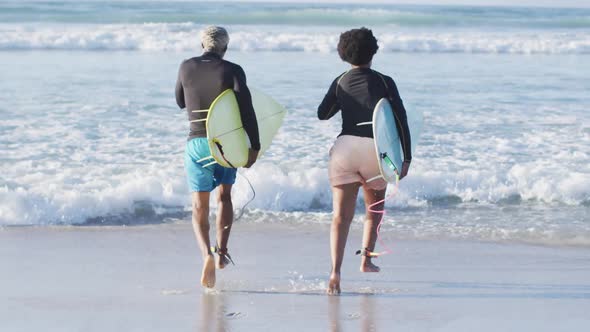 Happy african american couple running with surfboards on sunny beach