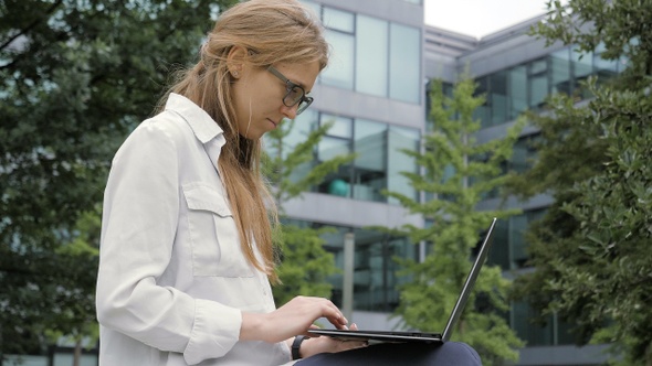 Young woman using laptop in the garden of office building.