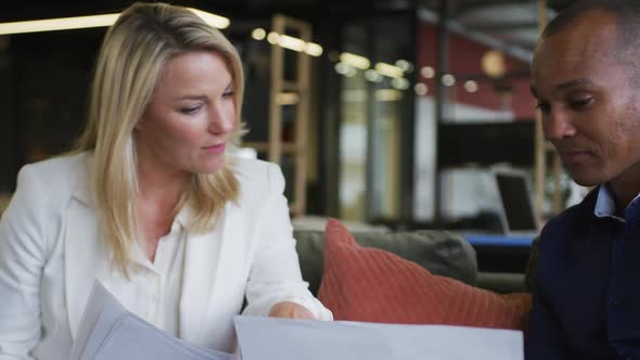 Two diverse business colleagues using laptop discussing paperwork and smiling during casual meeting