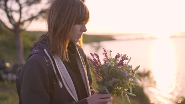 Beautiful Young Woman with a Bouquet of Wildflowers on the Coast at Sunset